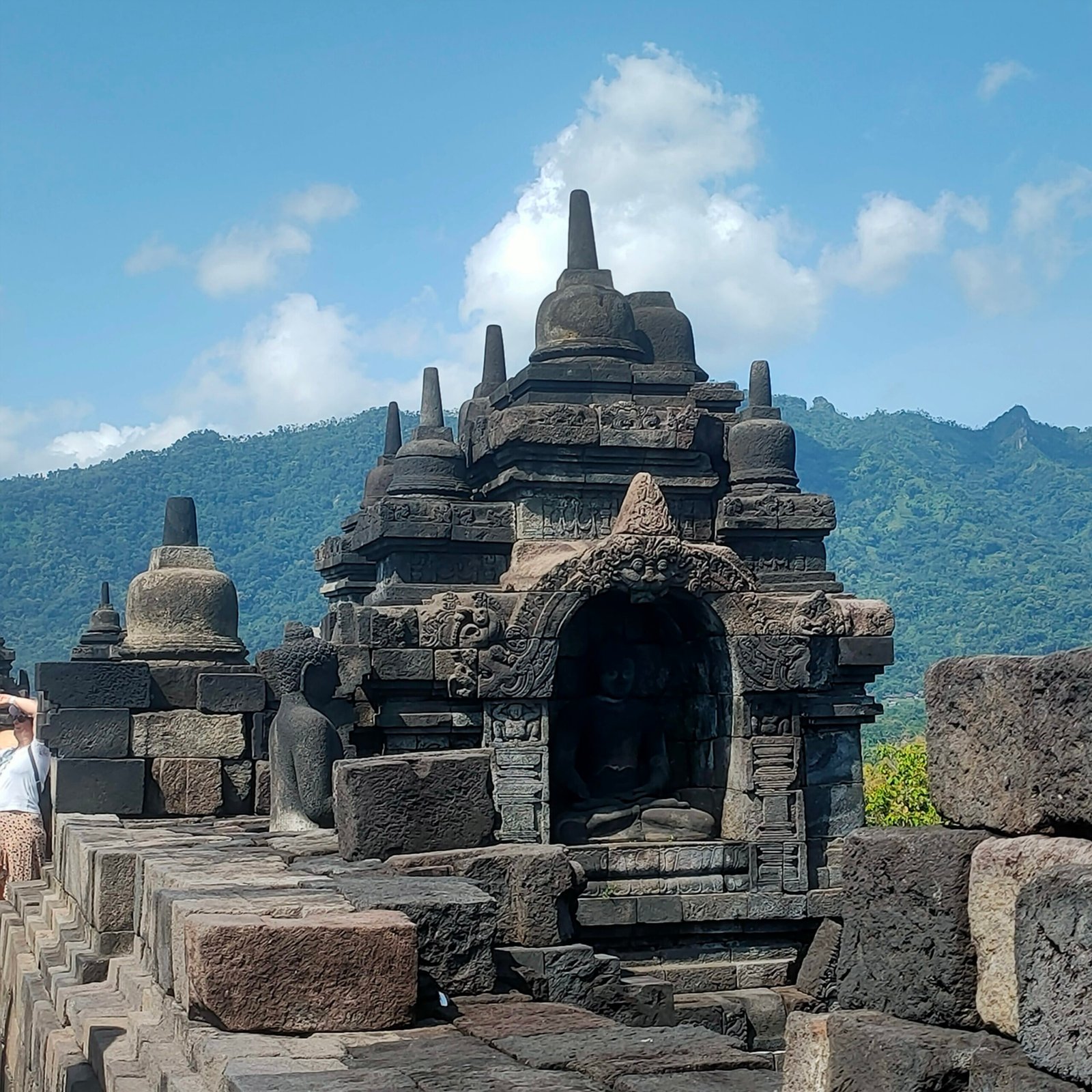 Square stone stupa shrine with arched doorway on Borobudur upper terrace with Mount Merapi volcano background Central Java Indonesia