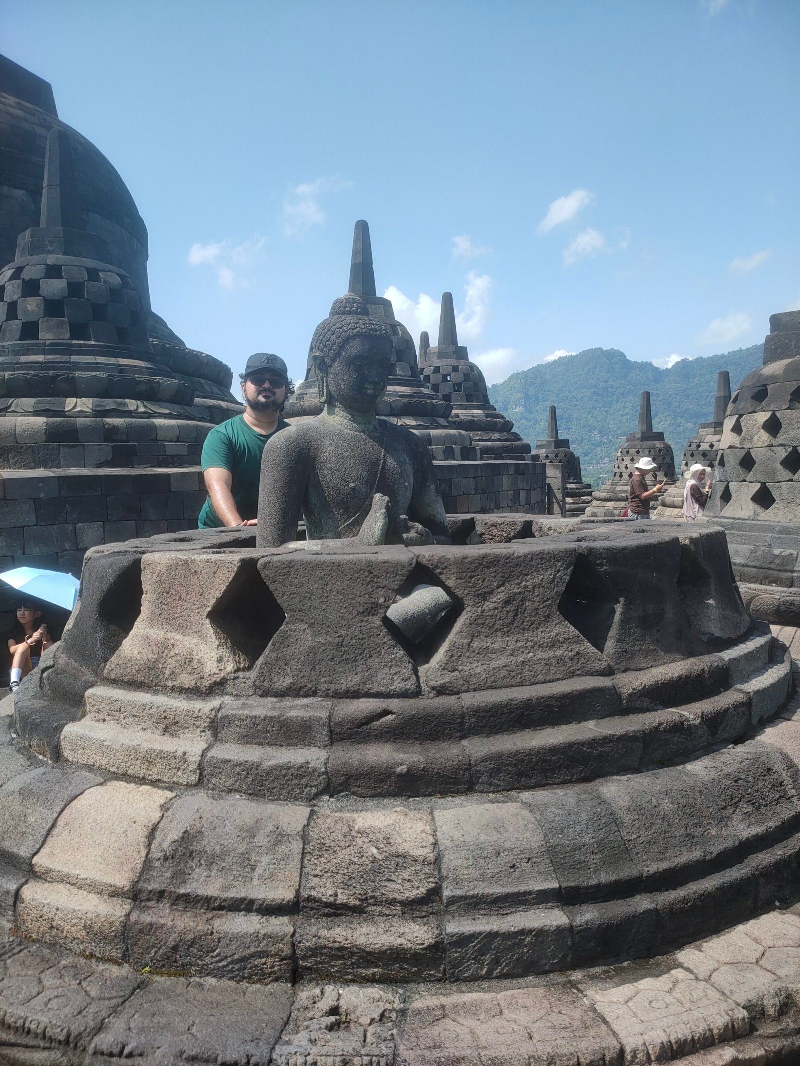 Borobudur Buddha statue inside diamond-patterned stone stupa with tourist in green shirt on upper terrace Central Java Indonesia