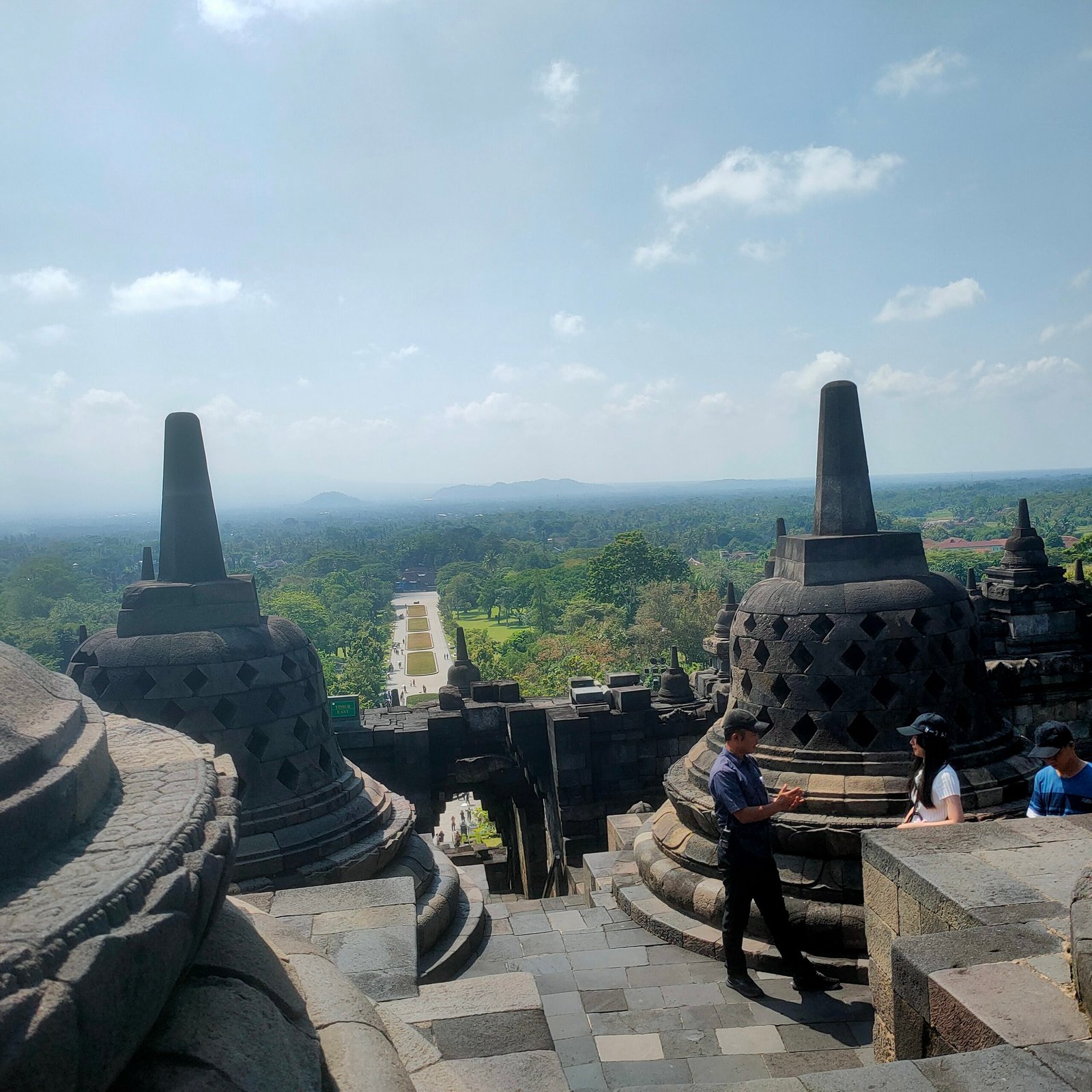 Borobudur temple view from upper terrace looking over green Central Java landscape with perforated stupas and security guard April 2026