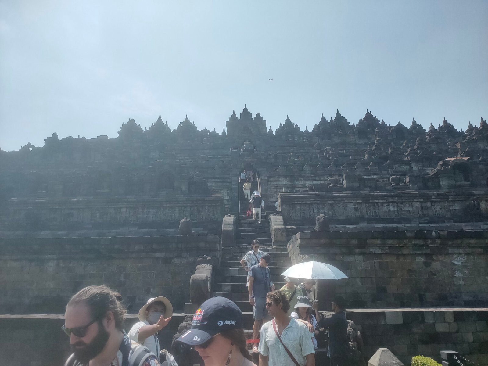 Borobudur temple tourists climbing stairs toward bell shaped stupas on upper terraces Central Java Indonesia April 2026