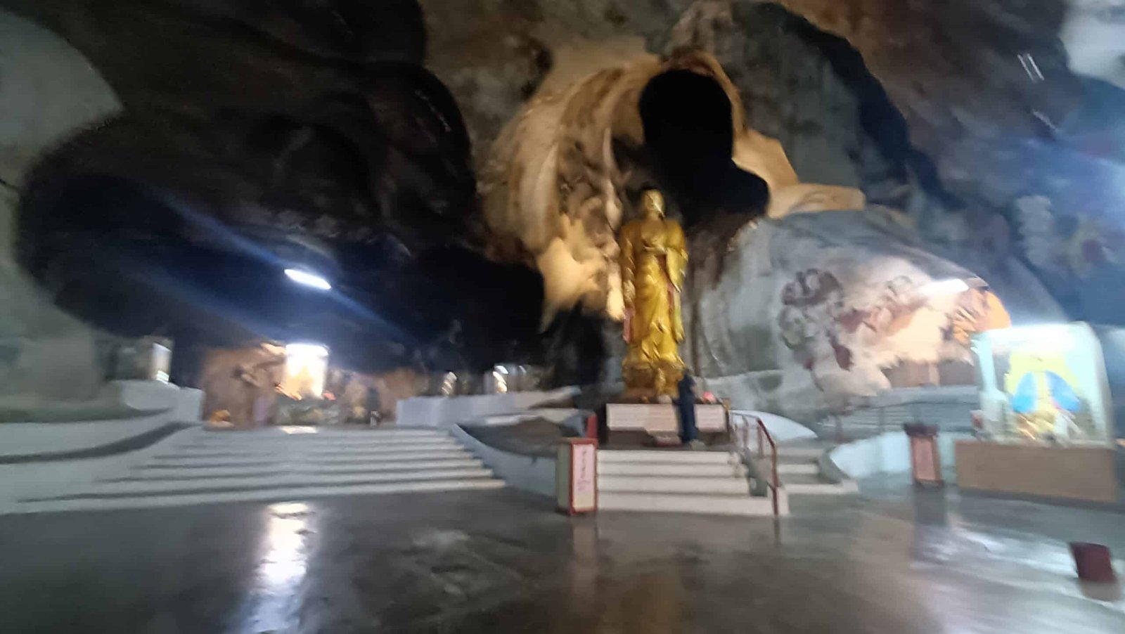 Golden standing Buddha statue on steps inside Perak Tong Cave Temple in Ipoh