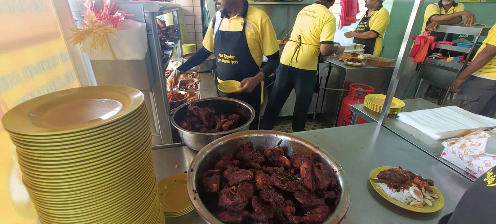 Yellow plates and curry trays at Nasi Ganja Ipoh with staff serving food
